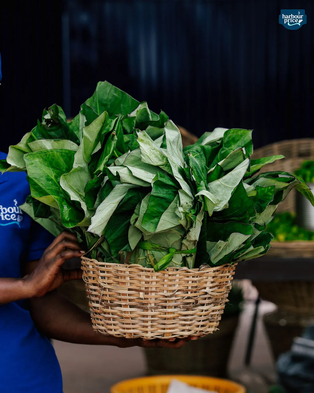 A staff member holds a woven basket overflowing with fresh leafy greens
